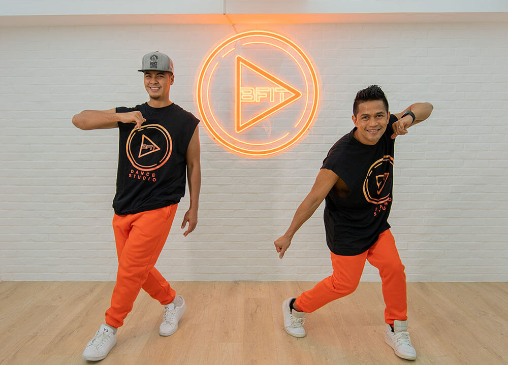 Two male dance teachers posing in the BFit Dance Studio next to the logo.